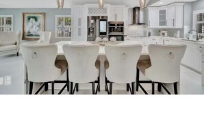 A modern kitchen with white cabinetry, a central island, pendant lighting, and a dining area with white chairs. - Welcome to your Private Tampa escape — designed for unforgettable group stays! (Tampa)