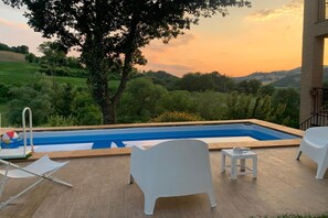 Ein Schwimmbecken mit Blick auf eine grüne Landschaft, einen Baum und einen weißen Stuhl.