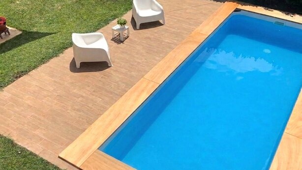 Ein rechteckiger Pool mit Holzterrasse und zwei weißen Liegestühlen.