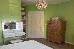 Ein Schlafzimmer mit einem Bett, einem Frisiertisch mit Spiegel, einer Holzkommode, einem Bücherregal und einer Tür.