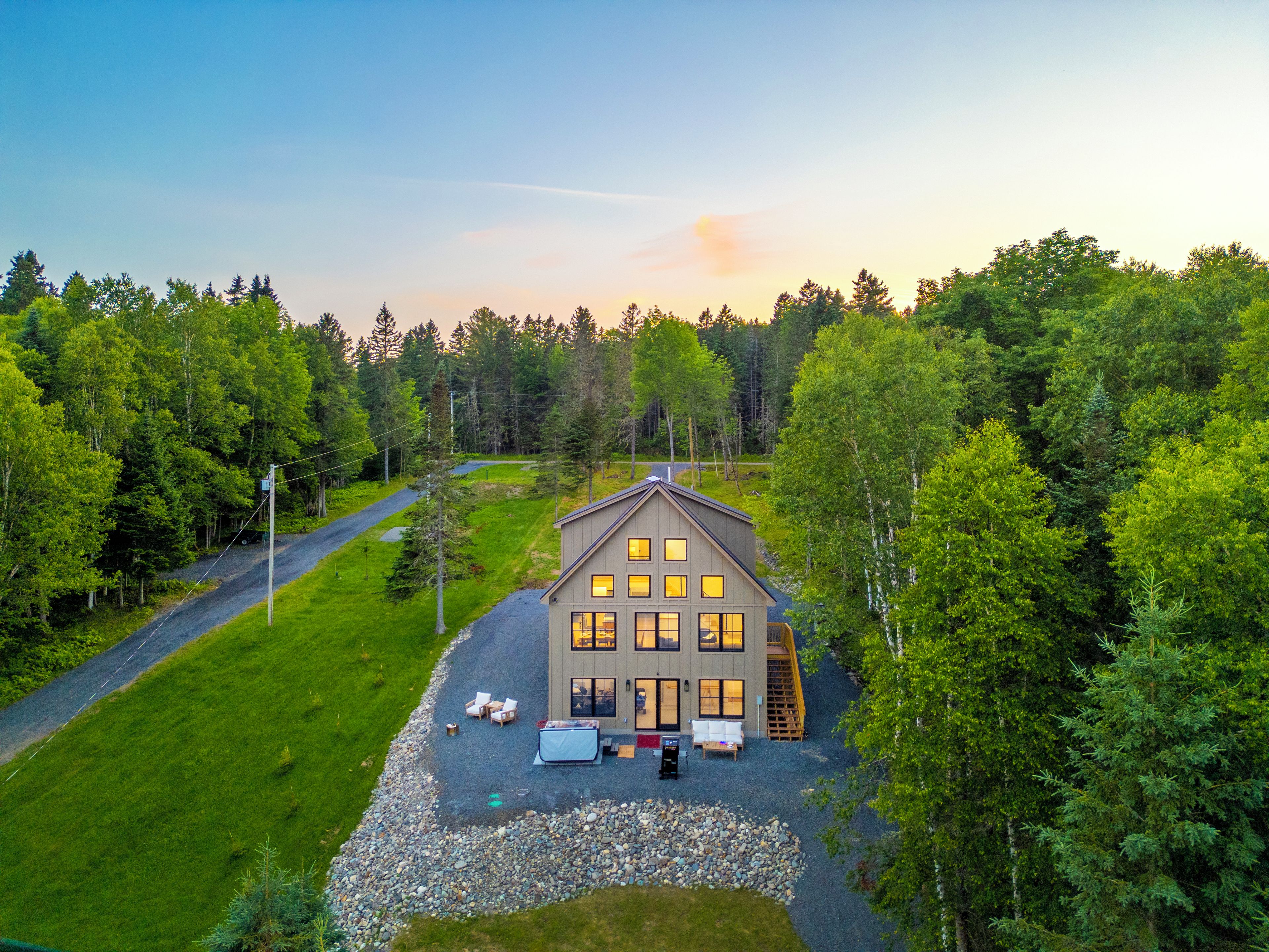 A two-story house with a driveway leading to a front porch, surrounded by a forested area.