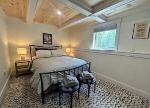 Ein Schlafzimmer mit einem Bett, Nachttischlampen, einem Fenster und einem gerahmten Bild an der Wand.