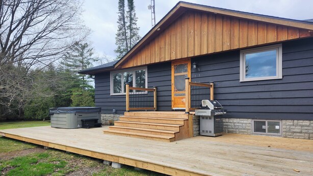A house with a wooden deck, a barbecue grill, and a hot tub.