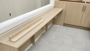 A room with a long wooden bench, light-colored cabinets, and a tiled floor.
