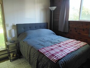 Ein Schlafzimmer mit einem Bett, einer Nachttischlampe, einem Nachttisch und einem Fenster.