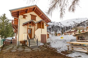 A chalet-style building with a wooden staircase leading to a door, surrounded by snow and mountains. - Le Vallon 2 - VALLOIRE (VALLOIRE)