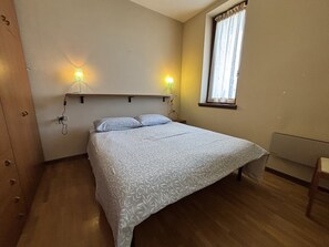 Ein Schlafzimmer mit einem Bett, zwei Nachttischlampen, einem Fenster mit Vorhängen und einem Holzboden.