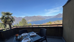 Une table dressée pour deux personnes sur un balcon offrant une vue sur les montagnes et un lac.