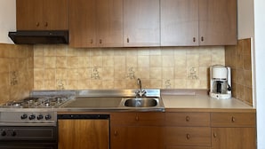 Une cuisine avec des meubles de rangement en bois, une cuisinière à gaz, un évier et une machine à café.