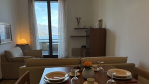 Un coin repas avec une table dressée pour quatre personnes, un canapé, une lampe et une vue sur les montagnes par la fenêtre.