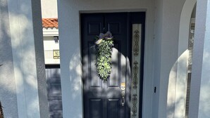 Een voordeur met een 'WELCOME' deurmat, een deurbel en een krans.
