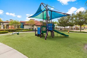 Un'area giochi con scivolo, strutture di arrampicata e una zona all'ombra.
