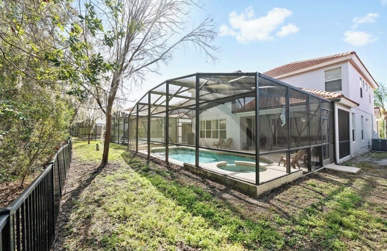 Ein Haus mit einem überdachten Pool, einem eingezäunten Garten und einem Baum.