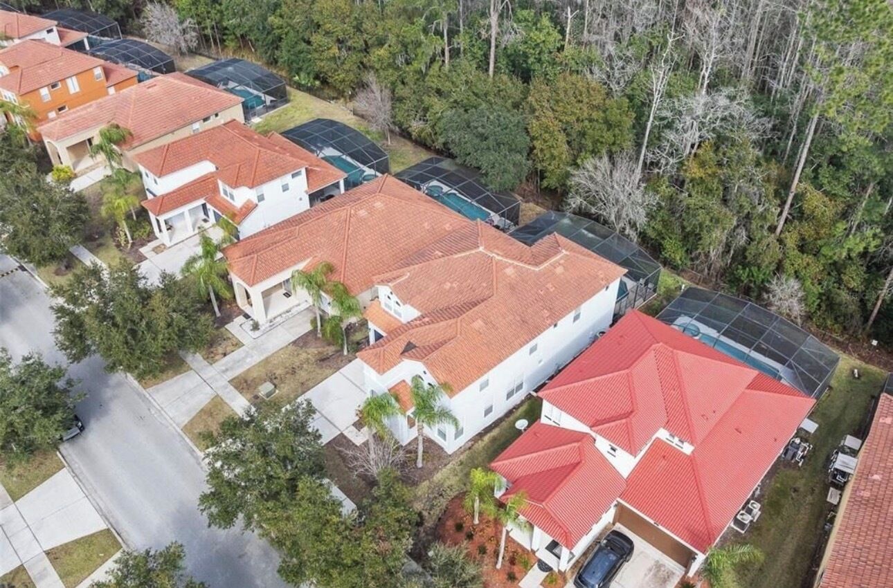 A residential area with houses featuring red-tiled roofs, surrounded by trees.
