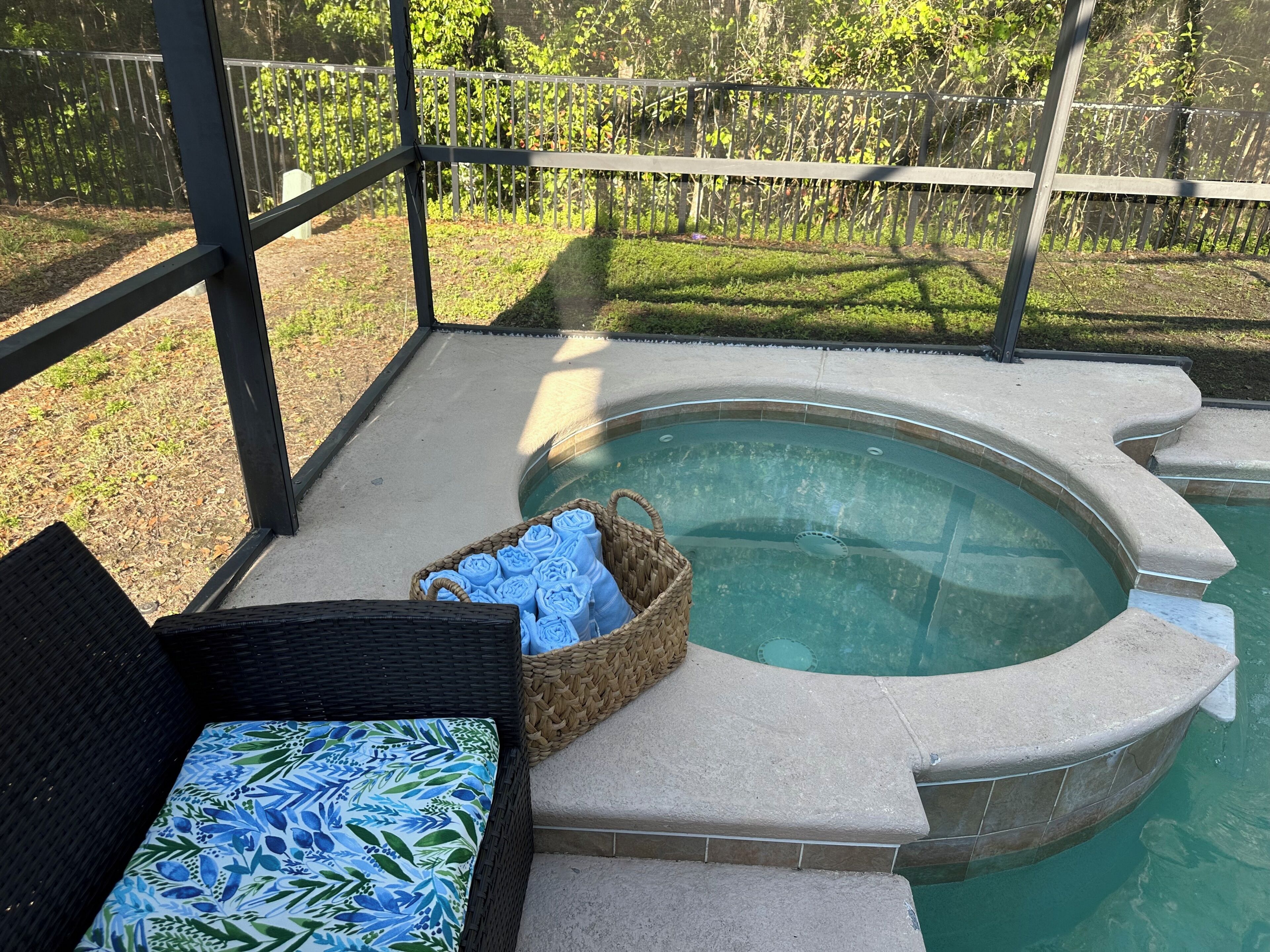 A covered outdoor area with a hot tub, wicker furniture, and a basket of towels.