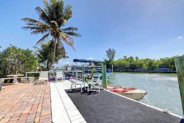 A dock with a boat, lounge chairs, and a palm tree.