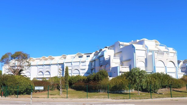 A large, white building with multiple balconies and arched windows, surrounded by greenery and a clear blue sky. - Studio Cabin with pools, parking, close to the sea and shops (LE GRAU DU ROI)