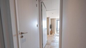 A hallway with a door, a wooden floor, and a view into a room with a window and curtains. - Water's Edge Wellness Retreat With Sauna (Workum)
