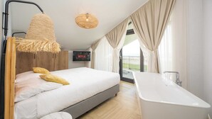 A modern bedroom with a bed, bedside table, and a large bathtub. - Water's Edge Wellness Retreat With Sauna (Workum)