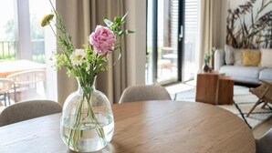 A round wooden table with a clear glass vase containing flowers. - Water's Edge Wellness Retreat With Sauna (Workum)