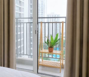Ein Balkon mit einer hölzernen Ablage, auf der ein Topfpflanze steht, mit Blick auf hohe Gebäude und einem Ausblick auf ein Schwimmbecken.