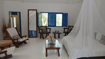 Una habitación con cama, una silla, una mesa, un espejo y una ventana con contraventanas azules.