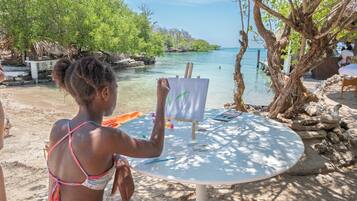A person painting at a beachside table with a view of the sea and trees.