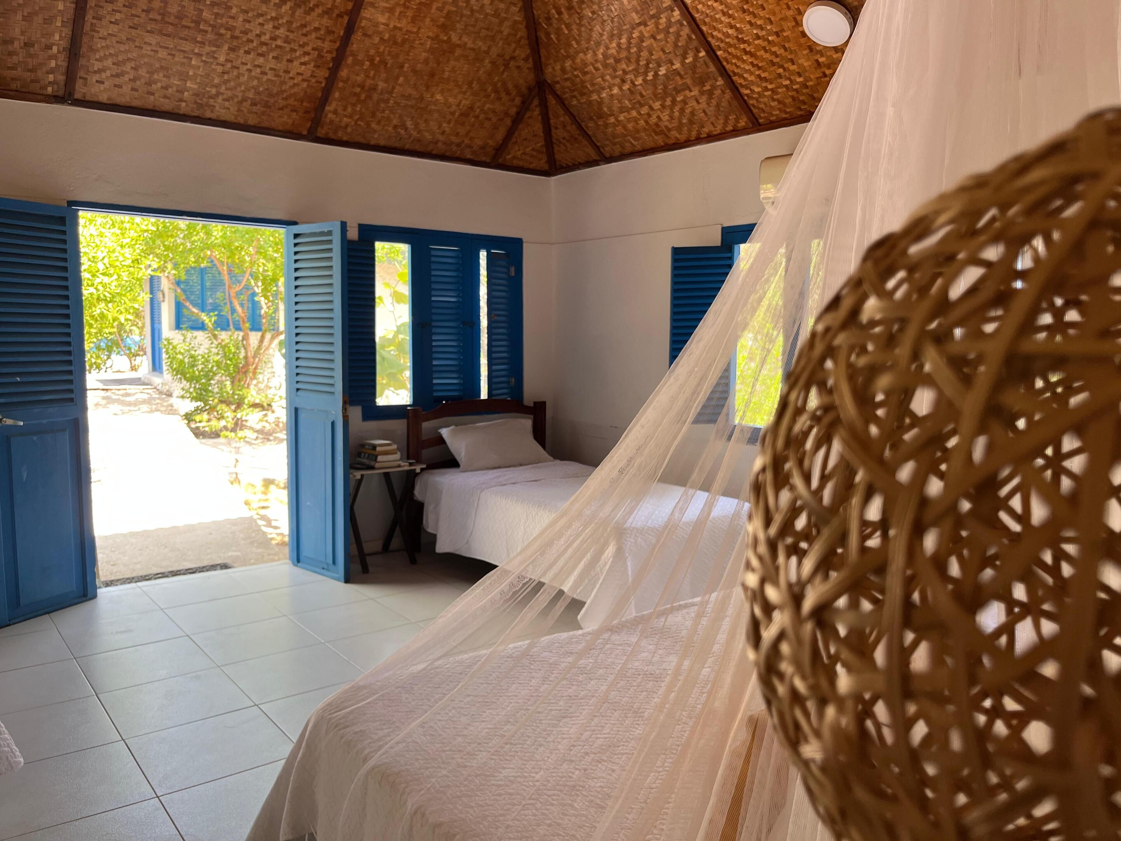 Una habitación con cama, una mesita y una ventana con contraventanas azules.