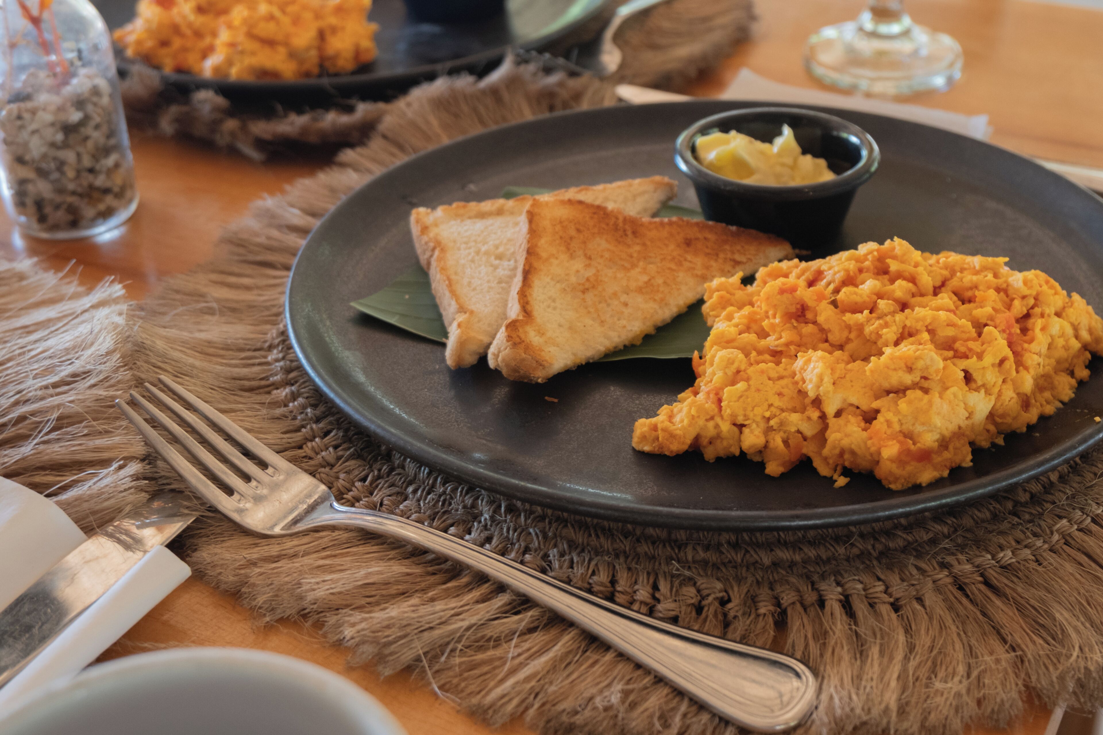 Un plato con huevos revueltos y tostadas sobre un mantel individual.