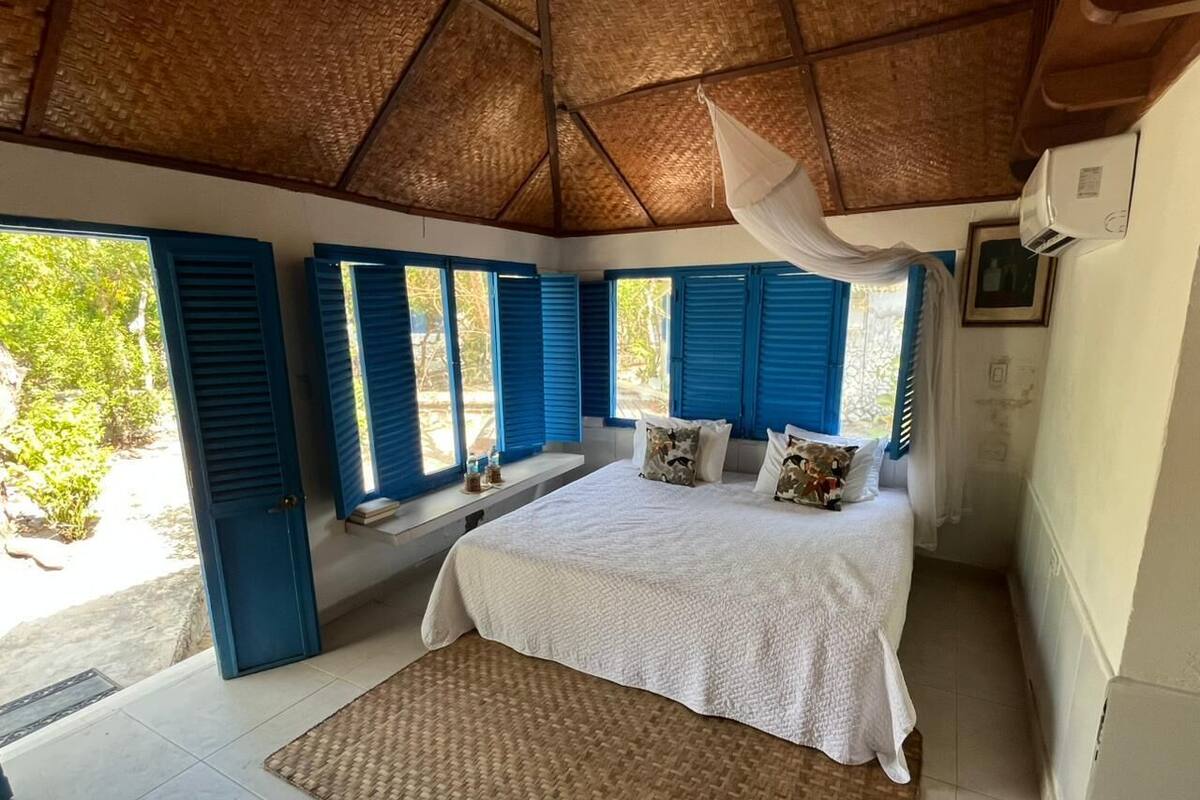 Une chambre avec un lit, un coin fenêtre, un ventilateur de plafond et une vue sur l’extérieur.