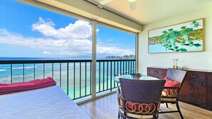Ein Balkon mit Blick auf den Ozean und die Stadtlandschaft, ein Essbereich mit Stühlen und Tisch sowie ein Bild an der Wand.