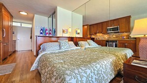 Ein Schlafzimmer mit einem großen Bett, Holzschränken, einem Fernseher und einer Küchenzeile.