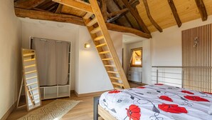 Un dormitorio con un entrepiso para dormir, una escalera de madera, una cama con colcha floral y una ventana con persianas.