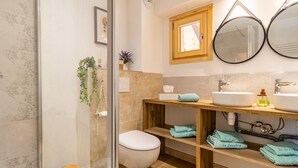 Un baño con cabina de ducha de vidrio, inodoro, lavamanos con espejo y repisas con toallas dobladas.