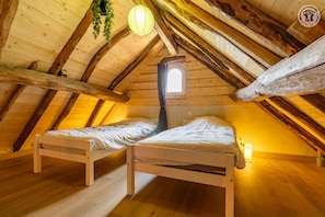 Ein gemütliches Schlafzimmer im Dachgeschoss mit zwei hölzernen Betten, einer hängenden Pflanze, einer Laterne und einem Fenster.