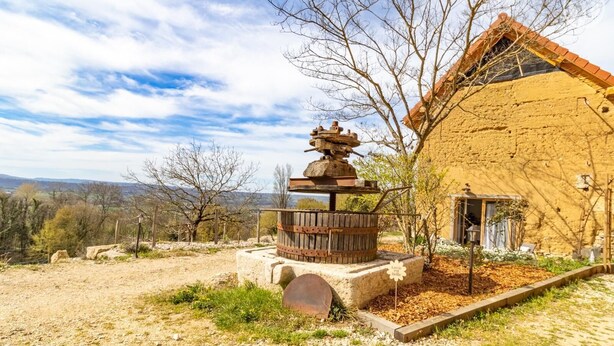 Un edificio rústico con un pozo de piedra, una estructura de madera encima y vistas al campo.