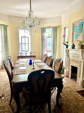A formal dining room with a chandelier, a fireplace, and a large window with curtains.