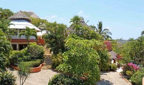 A resort with a thatched-roof building, a paved pathway, and lush greenery.