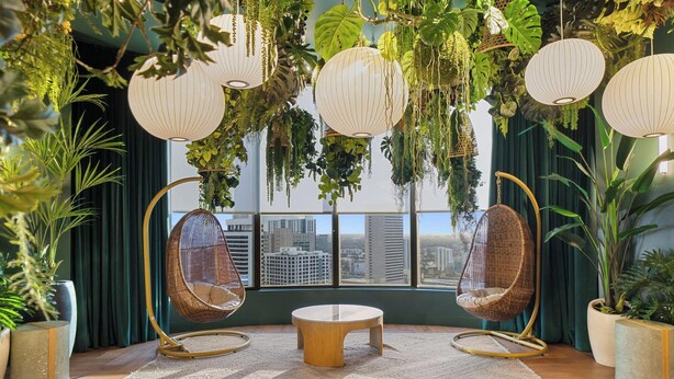 Ein Zimmer mit zwei Hängestühlen, einem runden Tisch und Blick auf eine Stadtkulisse durch große Fenster.