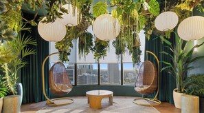 Ein Zimmer mit zwei Hängestühlen, einem runden Tisch und Blick auf eine Stadtkulisse durch große Fenster.