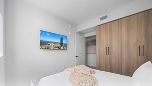 Une chambre à coucher avec un lit, une grande armoire en bois, un mur blanc orné d’un tableau encadré et un plafond blanc.