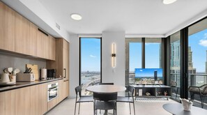 A modern kitchen with wooden cabinets, a dining area with a round table and chairs, and a large window offering a city view. - 501 First #3301|2BR w/ WaterView near Cruise Lines (Miami)