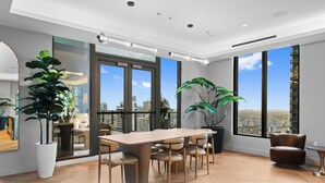 Een modern interieur met een grote eettafel, meerdere stoelen, grote ramen met uitzicht op de stad en potplanten.