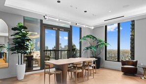A modern interior with a large dining table, multiple chairs, large windows with city views, and potted plants. - 501 First|Studio w/ Water View near Kaseya Center (Miami)