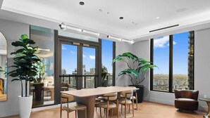 Un espace de bureau moderne doté d’une grande table, de chaises, de plantes en pot et de grandes fenêtres offrant une vue sur la ville.
