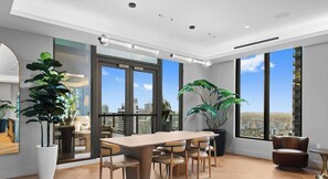 A modern office space with a large table, chairs, potted plants, and large windows offering a city view. - 501 First #2109|Miami City Downtown Studio (Miami)