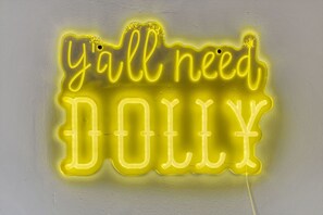 Ein Neon-Schild mit dem Schriftzug 'y'all need DOLLY' an einer schlichten Wand.