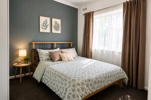 Een slaapkamer met een bed, een nachtkastje met een lamp, een potplant en twee ingelijste botanische prints aan de muur.