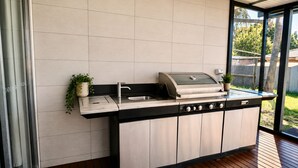 Eine moderne Außenküche mit Edelstahlgrill, Spüle und Schränken.