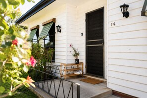 A white building with a black door, a number '14' on the wall, a bench, a potted plant, and a small table.